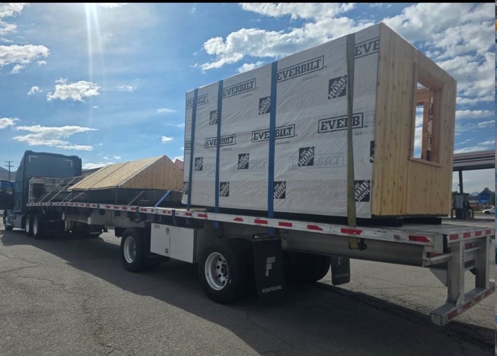 Flatbed trailer loaded with oversized modular wooden structures under a clear sky.