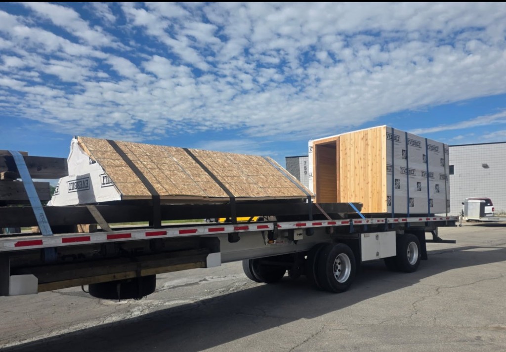 Flatbed trailer with roof section and modular unit wrapped for weather protection.