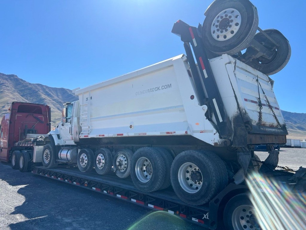 Heavy-duty dump truck loaded on a specialized lowboy trailer in bright daylight.