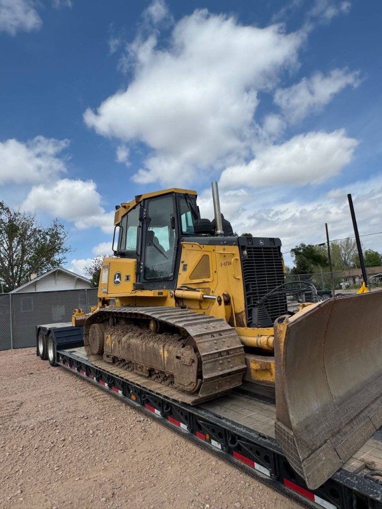 Side view of yellow crawler dozer on lowboy trailer with cab and blade visible.