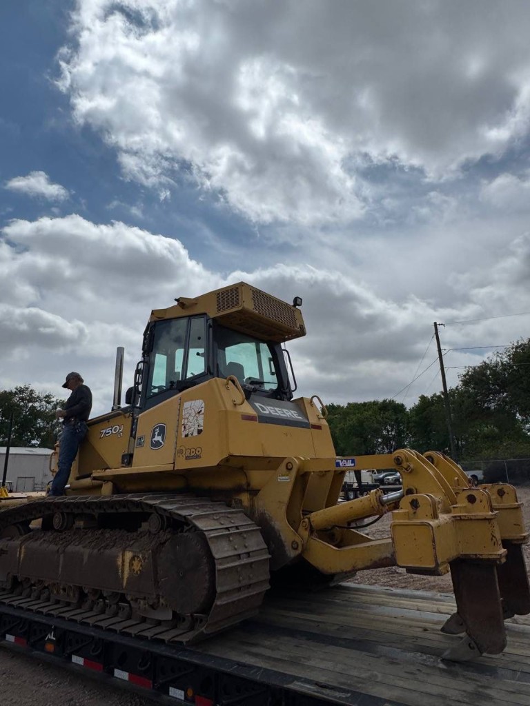 Crawler dozer on trailer with operator nearby for scale against a dramatic sky.