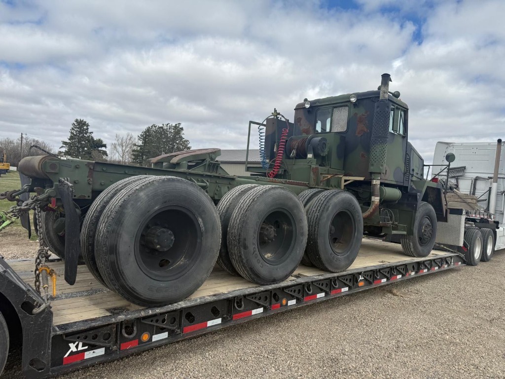 Side profile of military-style tractor on lowboy trailer with wooden deck.